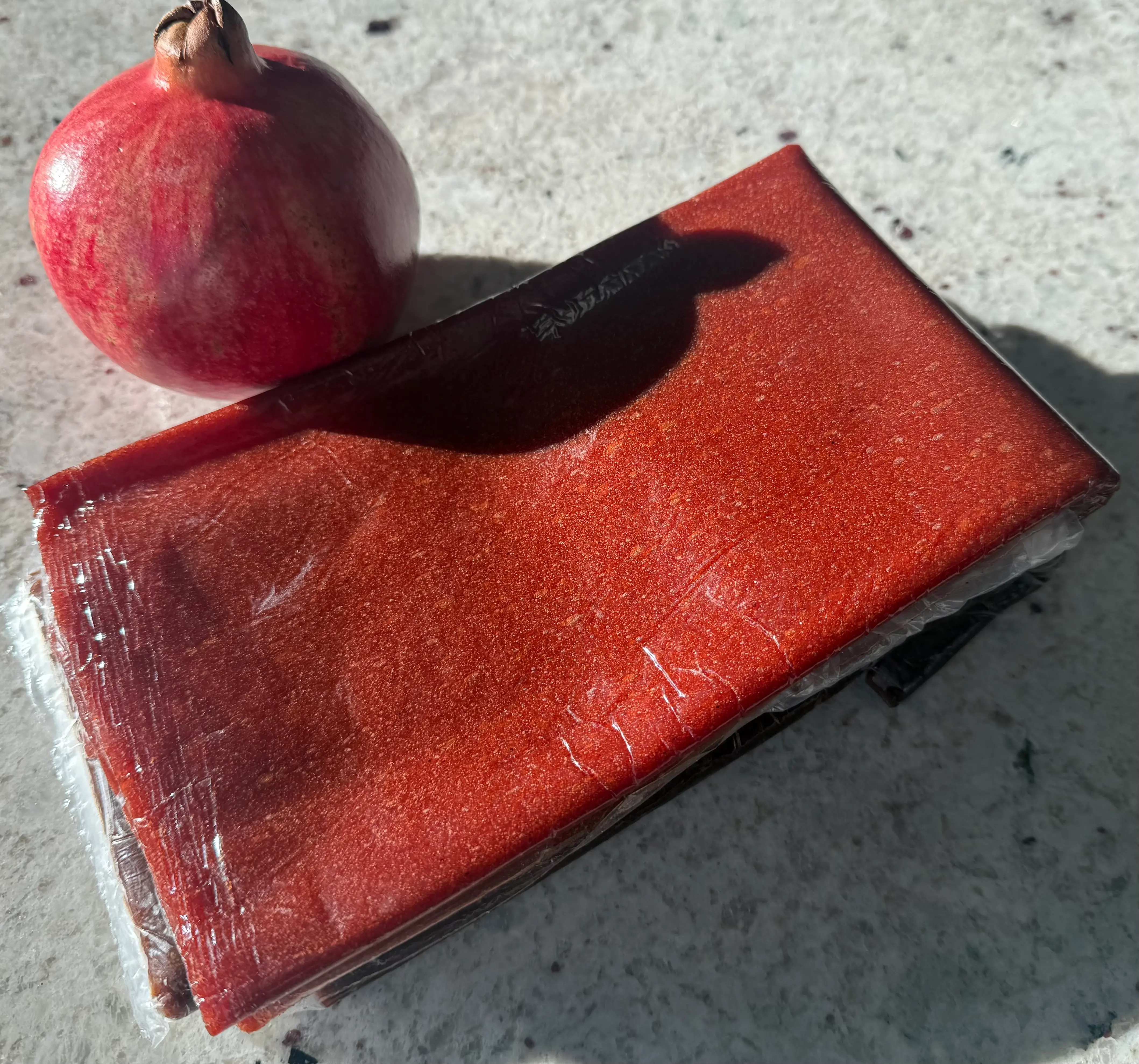  A picture of a fresh pomegranate fruit placed near 3 fruit leathers